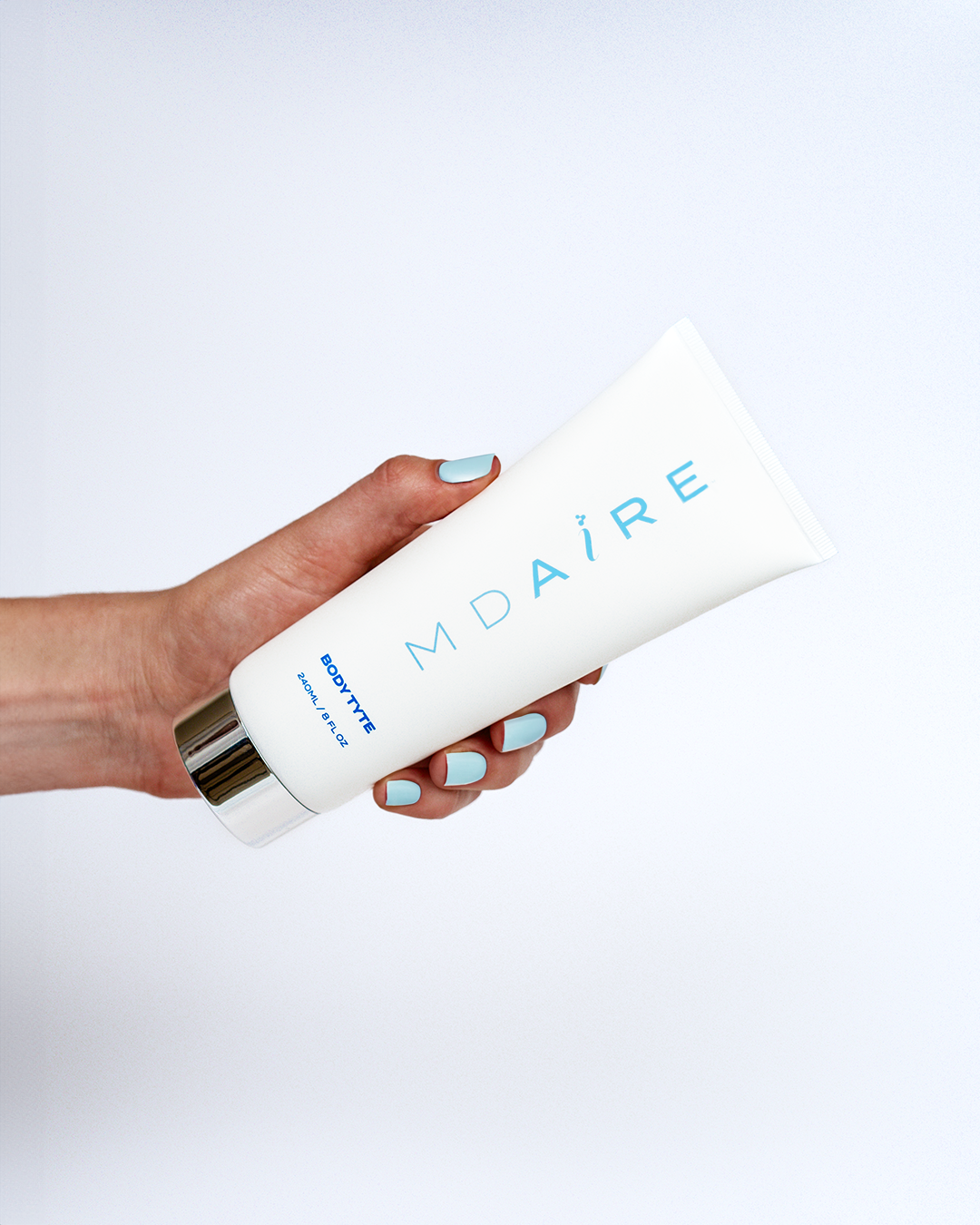 Hand holding Body Tyte tube with light blue logo and silver cap in gallery position 1 on white background
