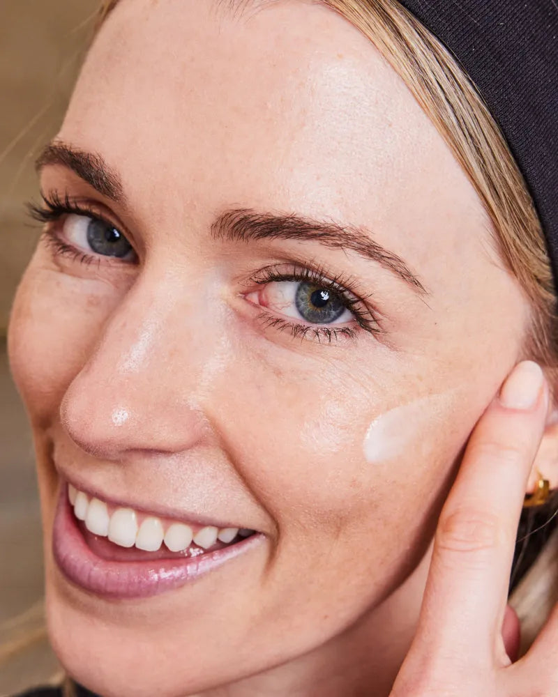 Close-up of smiling woman applying cream to cheek demonstrating Skinca