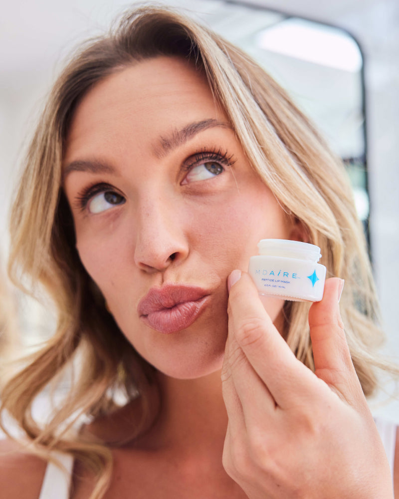 Woman holding Peptide Lip Mask jar close to face with a playful expression in gallery position 1