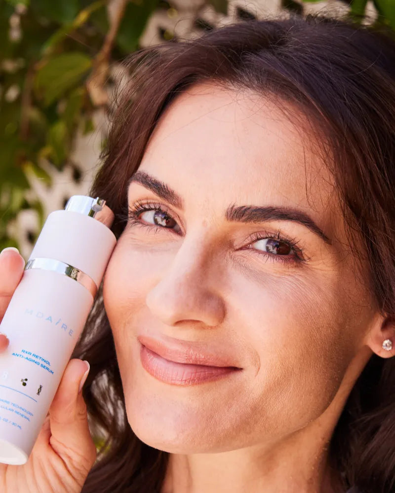 Close-up of woman smiling while holding MDAiRE RXR Retinol Serum from 