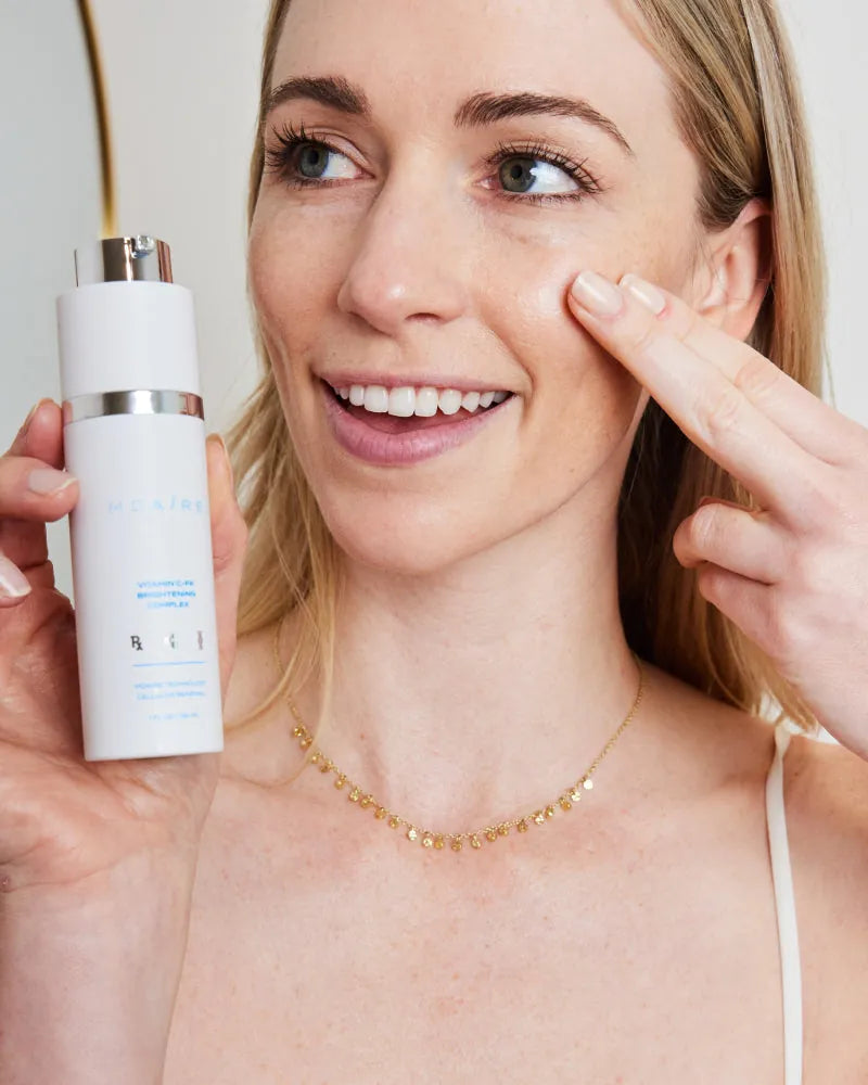 Smiling woman demonstrating Brightening Trio serum application to chee
