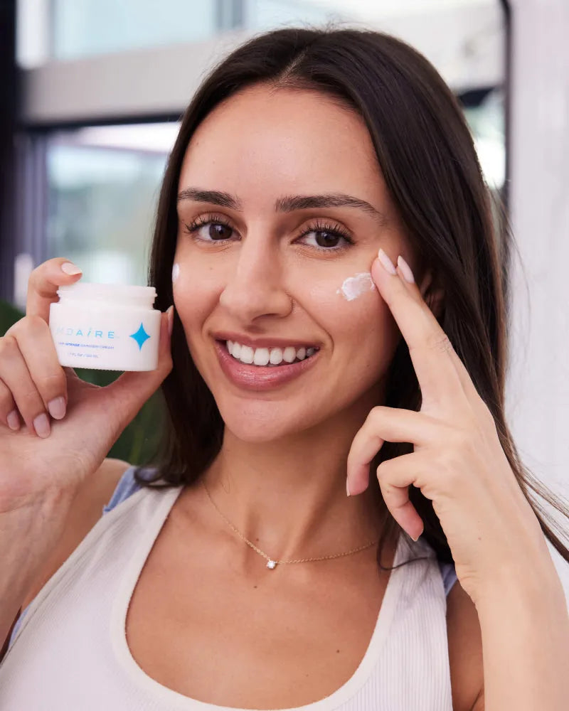 Woman smiling while applying NMF Intense Barrier Cream on cheek indoor